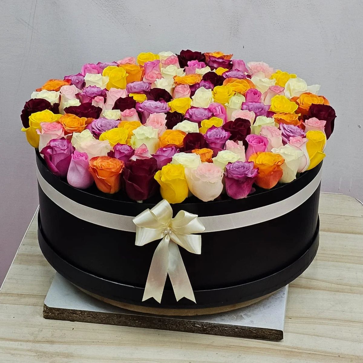 A beautiful pastel mix of pink, peach, yellow, and cream roses in an elegant box.